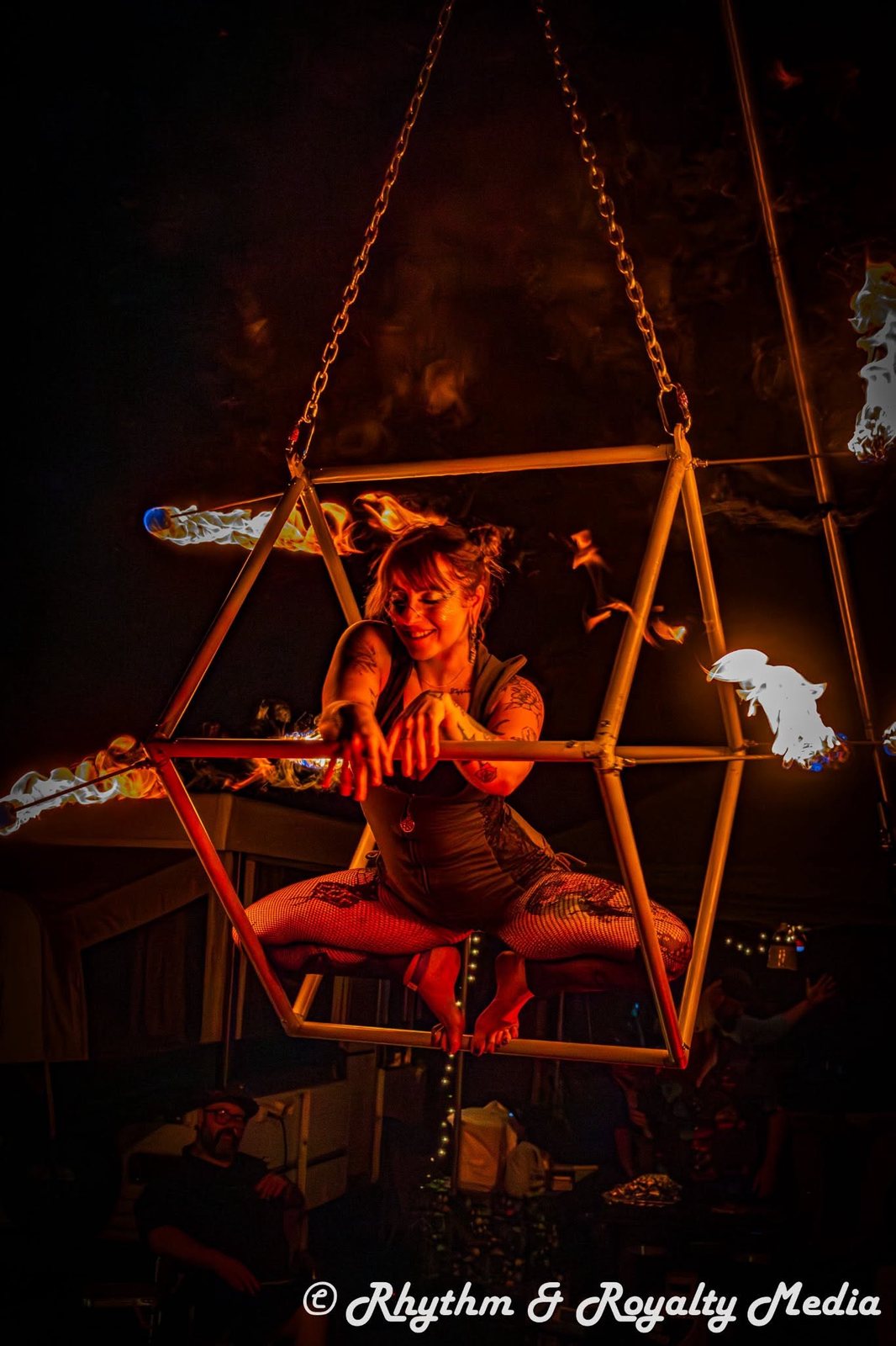 Performer posed in a hanging cube lit by fire